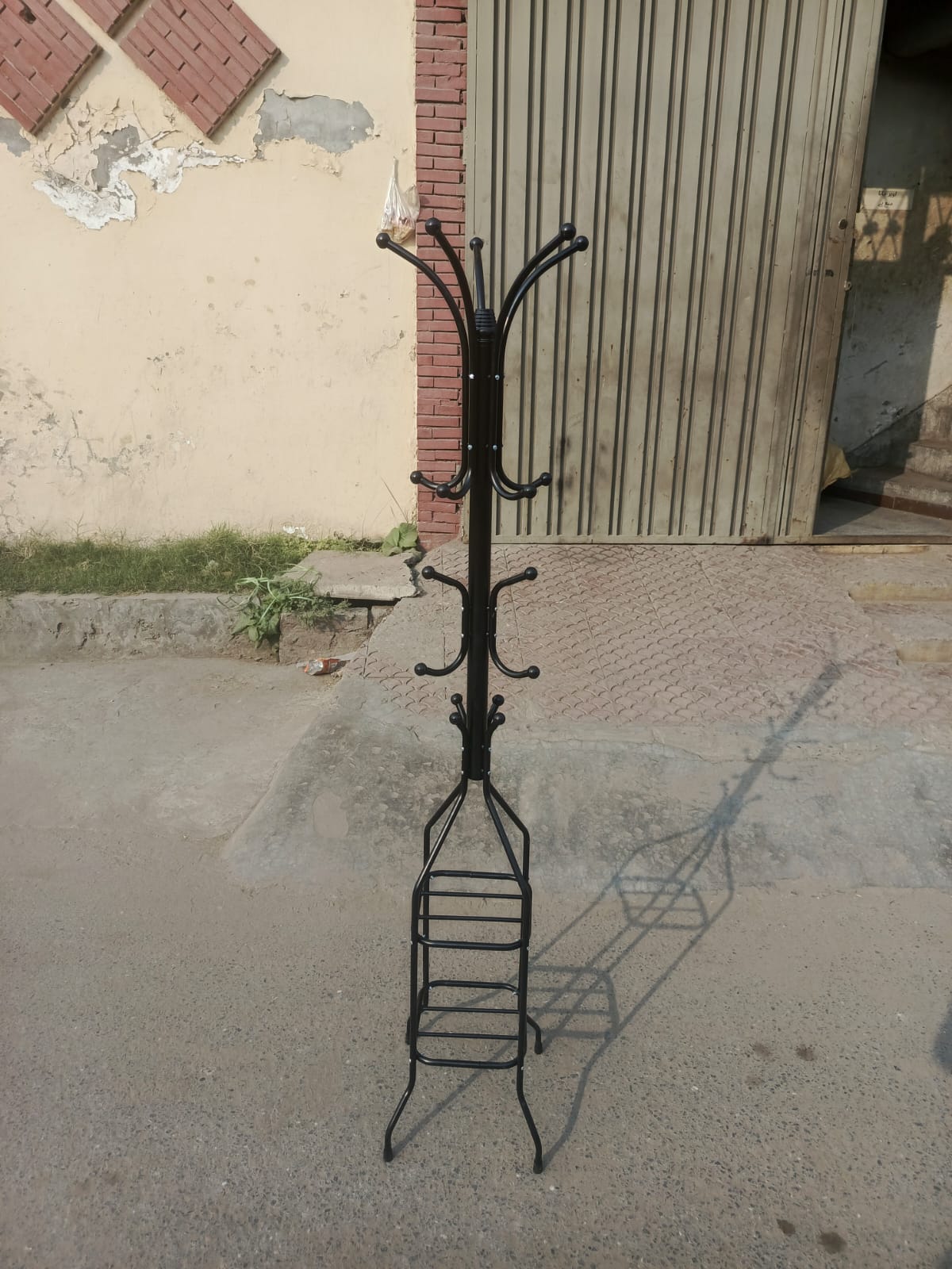 Black metal coat rack with multiple hooks on a concrete floor.