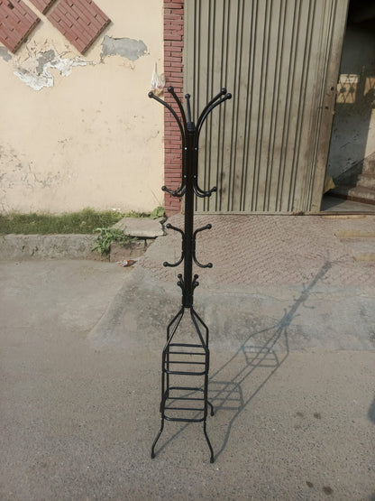 Black metal coat rack with multiple hooks on a concrete floor.